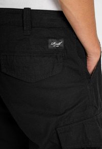 Pantalones cargo negros confeccionados con tejido texturizado, que cuentan con bolsillos laterales, un bolsillo trasero con etiqueta y detalles de costura visibles.