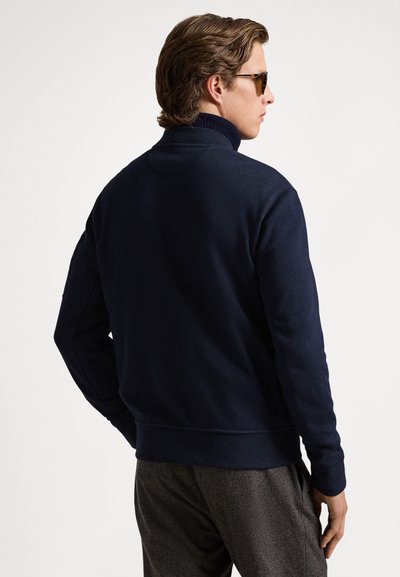 Μπλε φούτερ ναυτικού στυλ με ψηλό γιακά, διαθέτει ριμπ μανσέτες και τελείωμα. Μαλακή υφή, μινιμαλιστικός σχεδιασμός, απεικόνιση από την πίσω όψη.