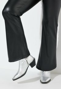 Pantalons évasés en simili cuir noir associés à des bottines métalliques argentées avec un talon bloc et des détails de fermeture éclair.