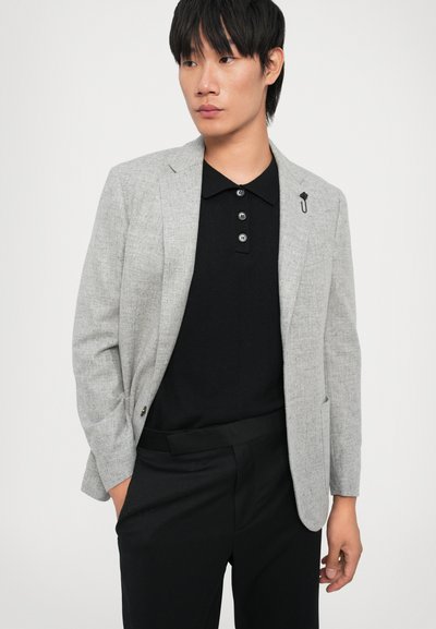 Grey blazer with a textured finish, single button, and a subtle pin detail, paired with a black polo featuring three-button placket.