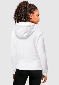 Fehér kapucnis pulóver húzózsinórral, bordás mandzsettákkal és alsó szegéllyel, sima textúrával és laza fazonnal, fekete leggings felett viselve.
