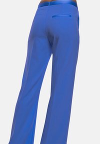 Pantaloni ampi blu realizzati in un tessuto liscio. Presentano una chiusura a zip e una tasca posteriore con un accento in satin.