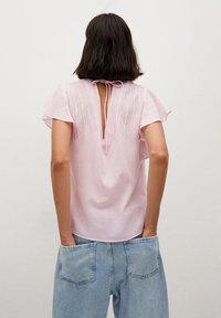 Lys pink bluse med flæseærmer, lukning med bånd i ryggen og lodrette striber. Sammen med løse blå denimjeans med store lommer.