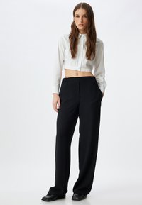 Witte cropped button-up blouse gecombineerd met zwarte wijde broek met een elastische tailleband, gladde textuur en zonder zichtbare patronen.