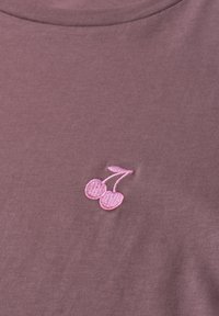 Gros plan sur un tissu mauve avec un petit motif rose brodé de deux cerises avec tiges et feuille près d’un col arrondi.