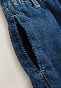 Jeans iz denima temno modre barve, ki vsebujejo vidne šive, otvoritev za žep in rahlo teksturirano površino. Povečana vzdržljivost s klasičnim dizajnom.