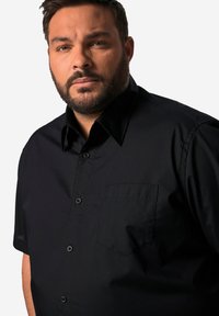 Svart kortärmad skjorta i slät tyg, med knapp-stängning, vänster bröstfick och spetsig krage.