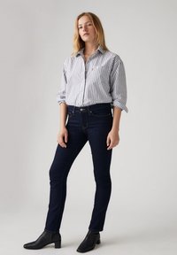 Camisa de botones a rayas blancas y marinas combinada con jeans de mezclilla oscuros y botines negros de tacón. Diseño simple, ajuste a medida, texturas suaves.