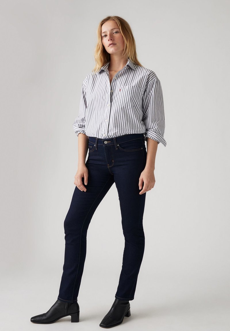 Camisa de botones a rayas blancas y marinas combinada con jeans de mezclilla oscuros y botines negros de tacón. Diseño simple, ajuste a medida, texturas suaves.