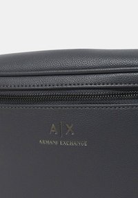 Borsa in pelle grigia con superficie testurizzata, chiusura con zip e logo in rilievo dorato: "A/X ARMANI EXCHANGE" sul davanti.