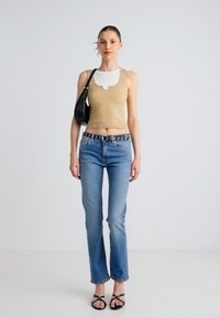 Beżowy prążkowany top na ramiączkach z falbankowym dekoltem, jasnoniebieskie jeansy, czarny pasek z okrągłymi ozdobami, czarna torba i czarne sandały na paski.