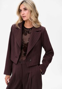 Brązowa krótka marynarka w prążki z klapami, z pojedynczym zapięciem na guzik oraz teksturowanym wnętrzem. Połączona z pasującymi spodniami o wysokim stanie.