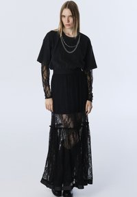 Zwarte gelaagde kant rok met een stevige onderlaag, gecombineerd met een losse zwarte t-shirt met korte mouwen en een kettingdetail rond de hals.