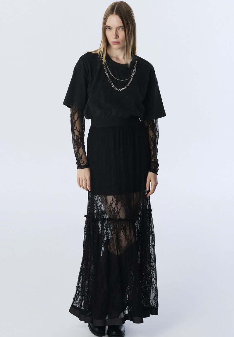 Zwarte gelaagde kant rok met een stevige onderlaag, gecombineerd met een losse zwarte t-shirt met korte mouwen en een kettingdetail rond de hals.