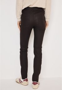 Zwarte skinny jeans met een gladde textuur, voorzien van achterzakken, riemlussen en minimale stikdetails. Gestyled met casual sneakers.