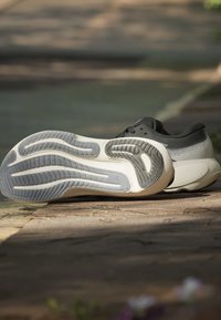 Chaussures de course avec semelles texturées grises et blanches posées sur un pavé en pierre sous la lumière du soleil en extérieur.