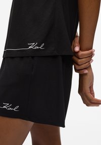 Sæt bestående af sort bomulds T-shirt og shorts, der har en buet kant og hvid kontrastsyning med 'Karl' logoet ved kanten af T-shirten og shortsene for detaljernes skyld.