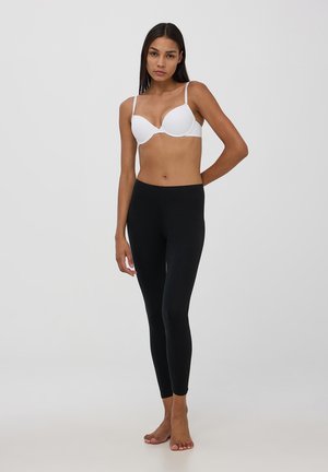 Leggings neri con un design aderente, abbinati a un reggiseno imbottito bianco. Tessuto liscio, senza motivi o decorazioni visibili.