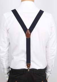 Navy stoffen bretels met bruin leren accenten, Y-vorm ontwerp, verstelbare metalen clips, gedragen over een wit shirt op een effen achtergrond.