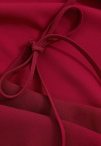 Nahaufnahme von burgunderfarbenem Stoff mit einer gebundenen Schlaufe, die die glatten und strukturierten Textilschichten hervorhebt.