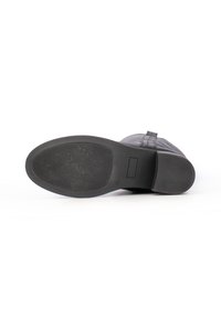 Suola in gomma nera di un boot, caratterizzata da una superficie testurizzata, punta arrotondata e tacco leggermente rialzato; design minimalista senza ulteriori decorazioni.