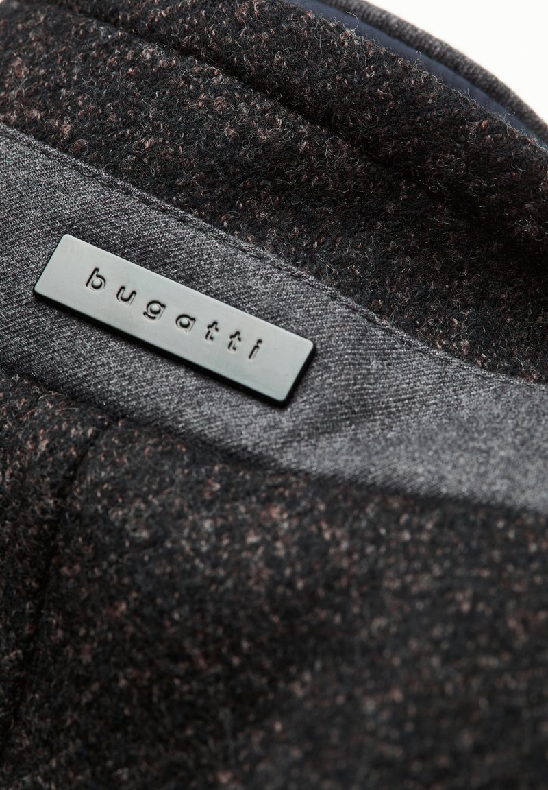 Tissu texturé noir et gris avec un mélange de fibres. Présente une étiquette en métal rectangulaire estampillée du nom de la marque "bugatti".