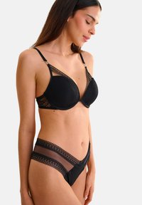 Soutien-gorge noir avec des garnitures en dentelle et des accents en mesh. Les bonnets ont une finition lisse, dotée de bretelles réglables et de fermetures à crochets. Culotte noir assortie avec des détails en dentelle similaires.