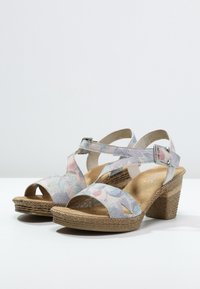 Kenkät, joissa on kukkakuosi vaaleissa väreissä, pehmeä pohja ja kudottu kanta lisäämässä rakennetta ja tukea.