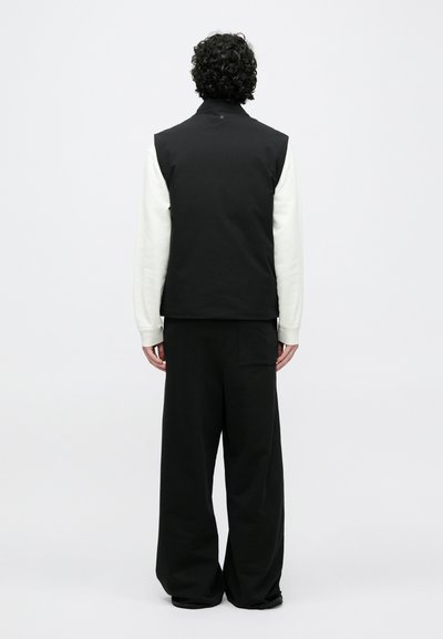 Fekete mellény magas nyakkal, fehér, hosszú ujjú inggel párosítva. A szettet laza fekete nadrág egészíti ki, mely zsebbel rendelkezik.