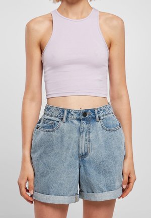 Vrouw draagt een mouwloos lila crop top en lichtblauwe denim shorts met hoge taille en opgerolde zoom, staand tegen een effen achtergrond.