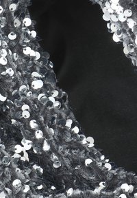 Pailletten-Stoff mit silbernen runden Pailletten auf einem dunklen Hintergrund. Die Textur ist plüschig mit einer glänzenden, reflektierenden Oberfläche.