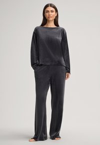 Donkergrijze lounge set gemaakt van zachte fluwelen stof. De top heeft een brede halslijn en lange mouwen, gecombineerd met loose-fitting broek.