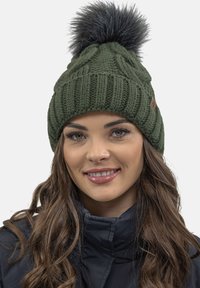 Gorro de punto verde oliva con textura acanalada y un gran pompón de piel sintética negra en la parte superior. Presenta una pequeña etiqueta de cuero marrón con el logo.