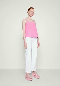 Top rosa sem mangas, de corte descontraído, combinado com calças brancas de perna larga. Modelo usa sandálias de bloco rosa com detalhes translúcidos.
