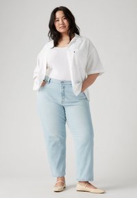 Camisa blanca de manga corta con botones, camiseta blanca sin mangas, jeans rectos de mezclilla azul claro y bailarinas beige, mostrando un ajuste relajado y un estilo casual.