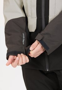 Veste imperméable avec une combinaison de couleurs noir et gris clair, poignets en Velcro et marquage "W-PRO 10000" sur la manche.