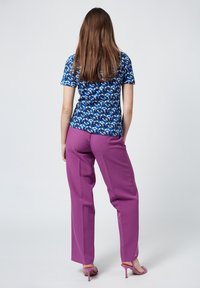 Blue patterned short-sleeve top paired with high-waisted, loose-fitting purple trousers. The model wears pink heels, seen from the back.