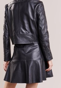 Zwarte leren cropped jack met gestikte details op de mouwen, gecombineerd met een zwarte leren uitlopende rok. Gladde textuur, verfijnde pasvorm.