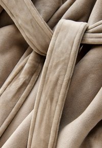 Accappatoio in fleece beige con una morbida e pelosa texture. Presenta una cintura da annodare e un design frontale sovrapposto per una chiusura sicura.