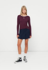 Bordo rebrasti longsleeve top s bijelim detaljima oko ovratnika, s "GAP" logotipom; u kombinaciji s mornarsko plavom plisiranom suknjom i crnim Converse tenisicama.