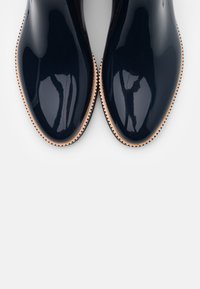 Zapatos de charol azul marino con un acabado liso y brillante y punta redondeada. Presentan un borde festoneado beige alrededor de la suela.