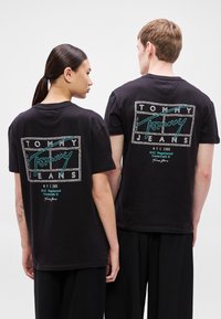 Czarne bawełniane koszulki z nadrukiem na plecach, przedstawiające "TOMMY JEANS" w turkusowym i białym kolorze, z logo w formie pudełka i dekoltem w serek.