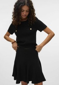 Robe en tricot noir à manches courtes, dotée de deux poches à rabat avec des boutons dorés et d'une jupe évasée. Texture lisse et corsage ajusté.