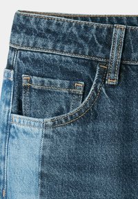 Gros plan sur un jean en denim montrant la poche avant, une petite poche à monnaie, une passants de ceinture et une couture contrastée avec deux nuances de tissu bleu.