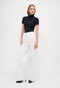 Top de cuello alto negro con canalé, combinado con pantalones blancos de pierna ancha de talle alto y tacones negros de punta. Diseño simple y limpio.