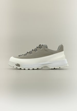 Alacsony szárú szürke-fehér sportcipő vastag talppal és fűzős kialakítással, oldalra fordítva, semleges háttéren.