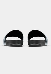 Sandales à glissière noires avec une texture lisse et deux larges sangles, avec trois rayures blanches verticales de chaque côté. Semelle plate.