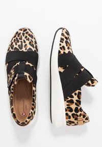 Leopardmønstret slip-on sko i blød pels med sort elastisk bånd hen over toppen og en hvid gummisål. Har en læderdetalje på bagsiden.
