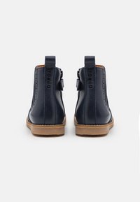 Námořnické kožené kotníkové boty s hladkým povrchem, zaoblenou špičkou a koňakovou gumovou podrážkou; mají poutka pro snadnější obouvání a dekorativní prošívání po stranách.