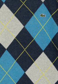 Tessuto a maglia con motivo argyle blu e crema su sfondo blu navy, caratterizzato da cuciture gialle e un piccolo logo verde.